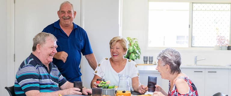 A group of seniors sitting around the coffee table laughing